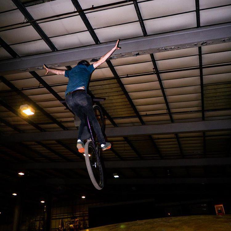 Bike rider in mid air with arms outstretched landing on airbag in a warehouse