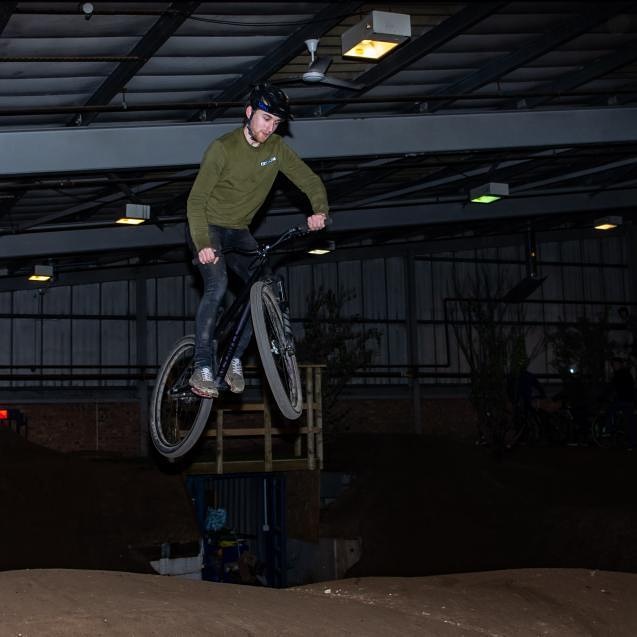 Bike rider in mid air over dirt jump inside a warehouse