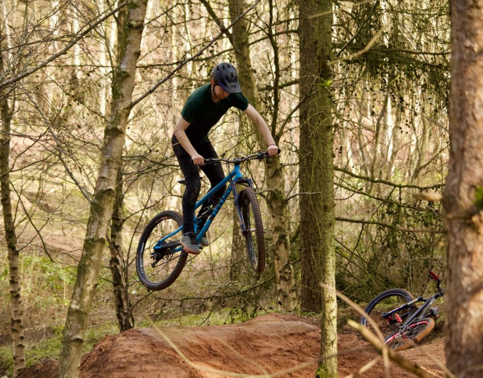 Mountain bike rider in mid air over a sandy jump in the woods