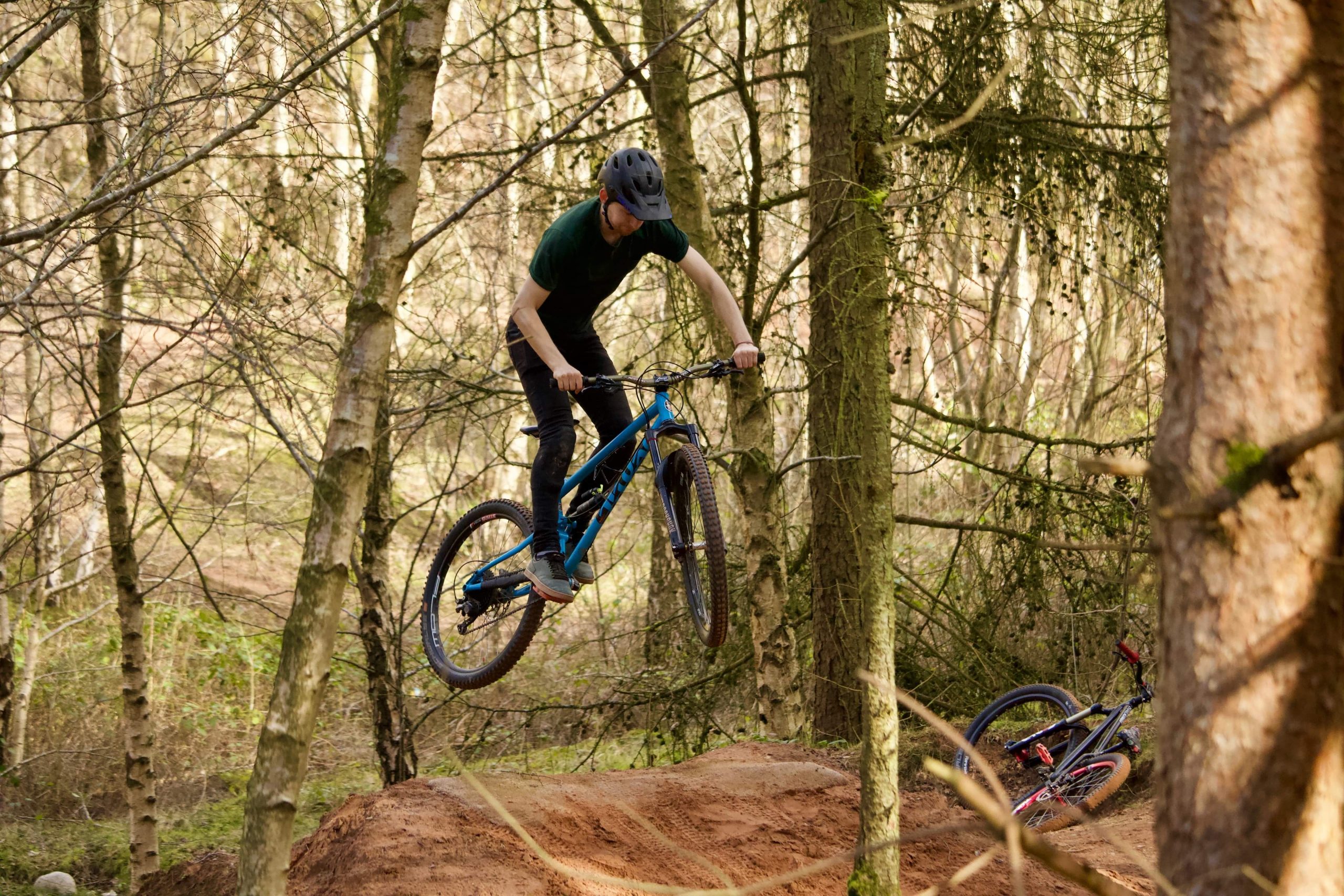 Mountain bike rider in mid air over a sandy jump in the woods
